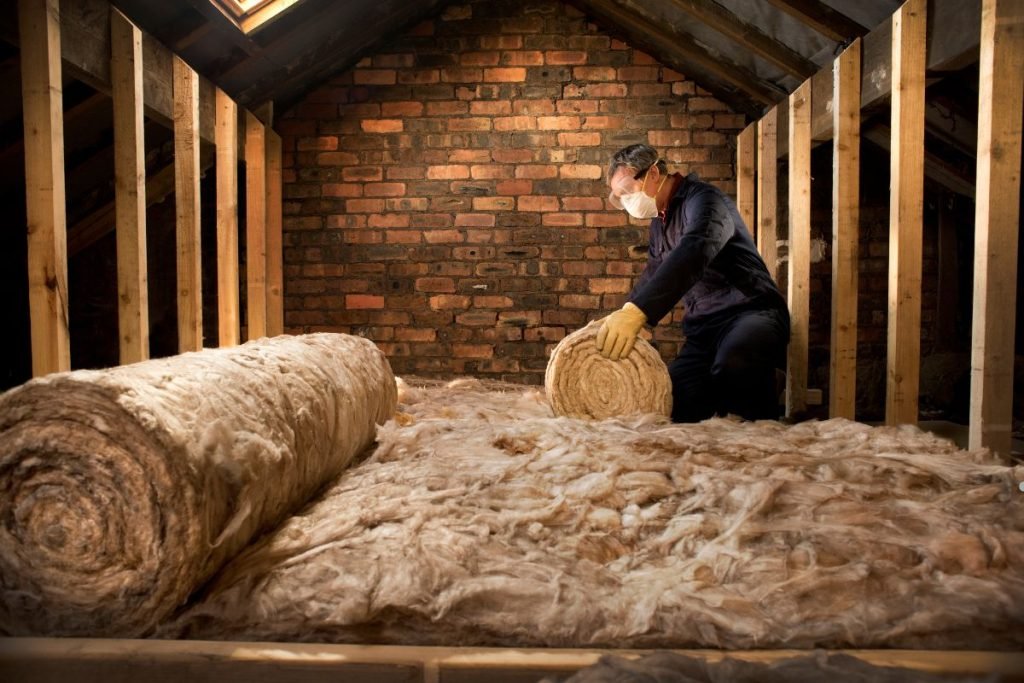 A man installs insulation in an attic, representing the services of the Best Insulation Company in Los Angeles.