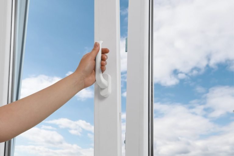 A person opening a window with a white handle, demonstrating the process of window insulation.